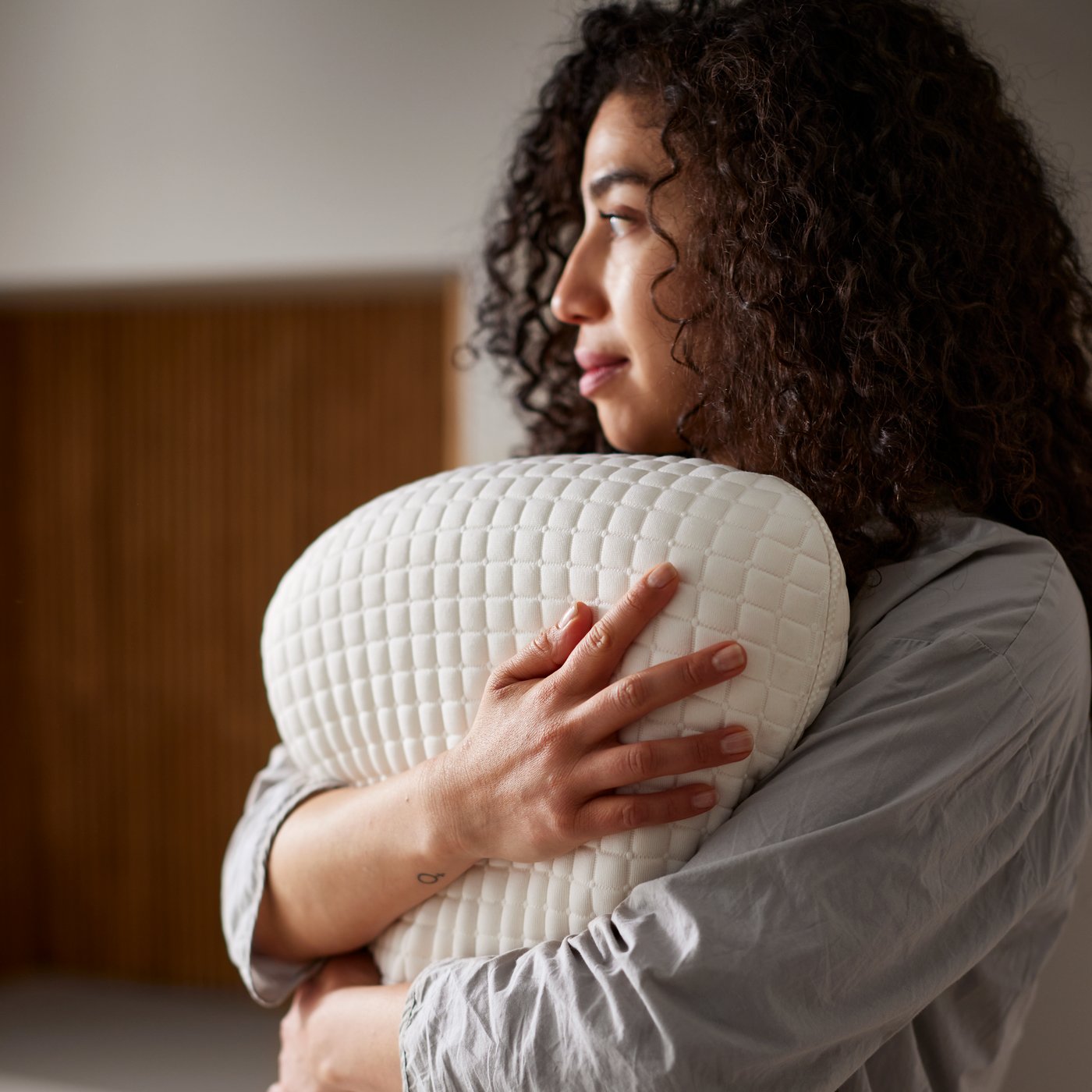 A person holding a KLUBBSPORRE ergonomic pillow for side and back sleepers to their chest.