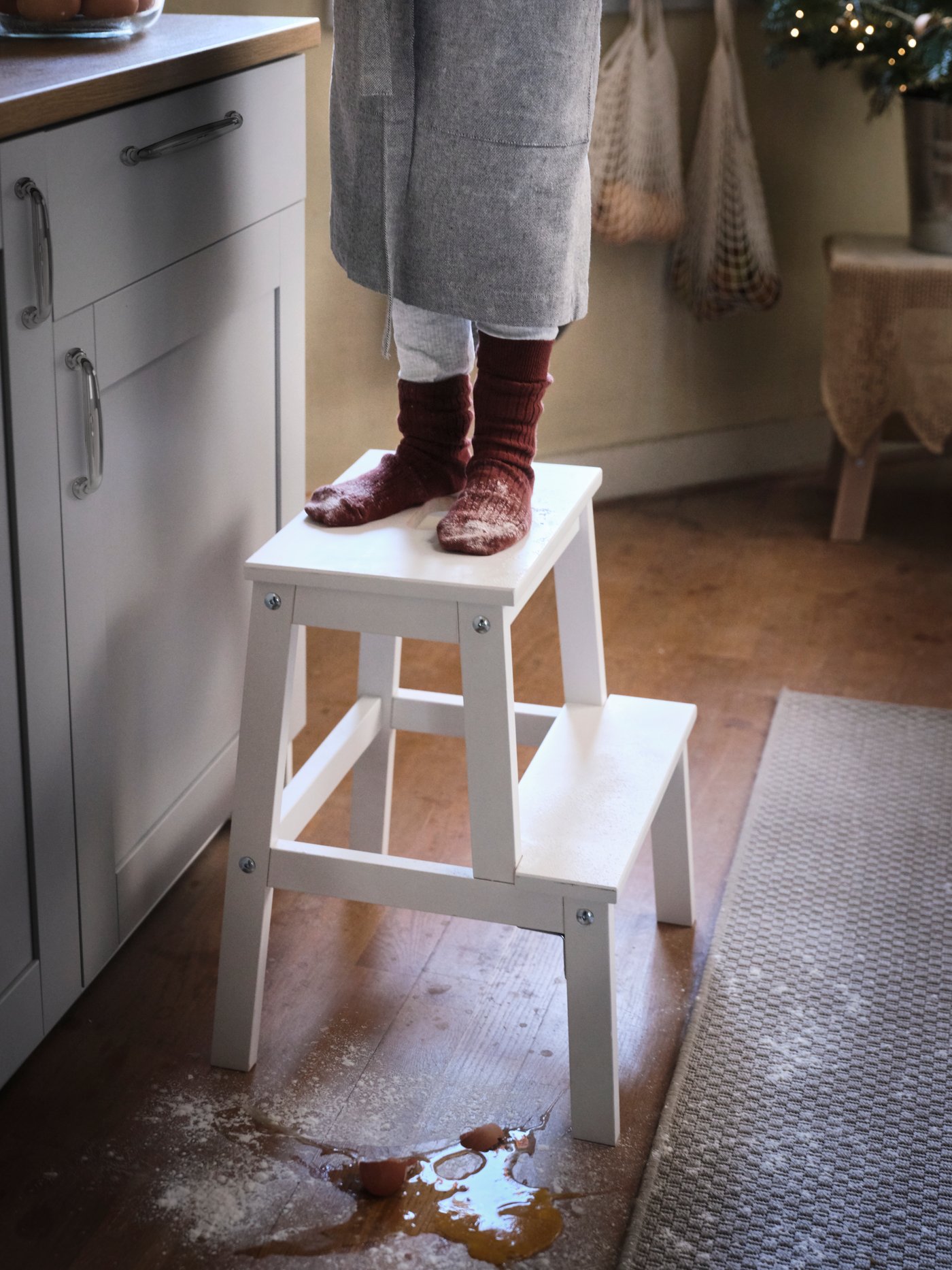 A child standing on a white BEKVÄM step stool in the kitchen. Something has been spilled on the floor.