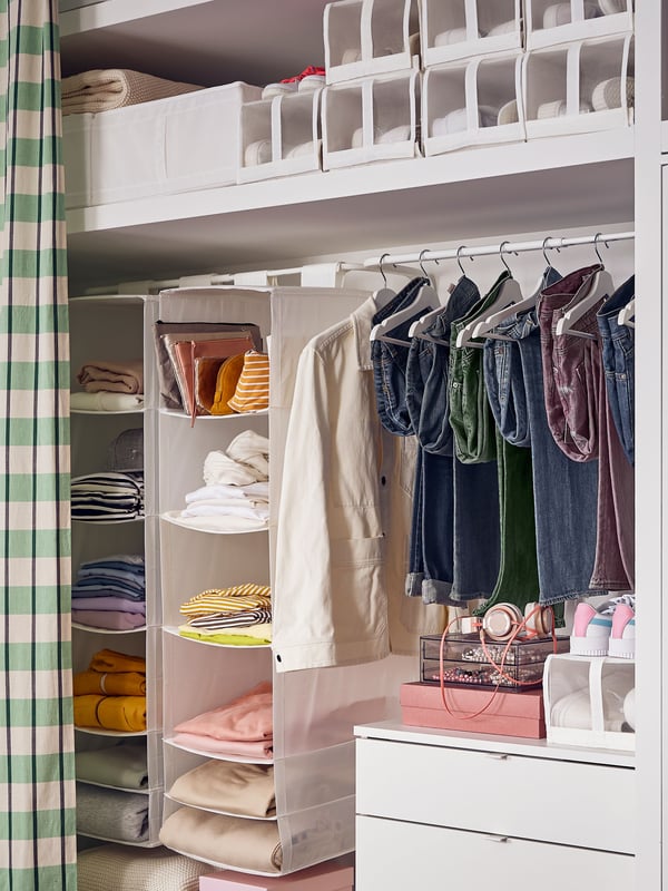 Es ist ein Kleiderschrank in einer Nische zu sehen, in dem Kleidung und Hängeaufbewahrungen mit Fächern an einer Kleiderstange hängen. Auf einem Boden befinden sich viele SKUBB Schuhboxen.