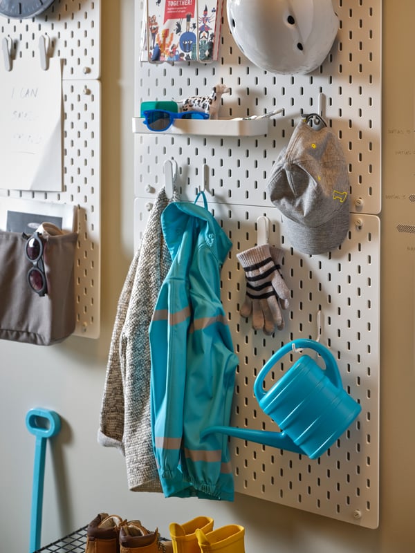 A section of hallway wall with SKÅDIS pegboards holding toys, clothing and other things at different heights.