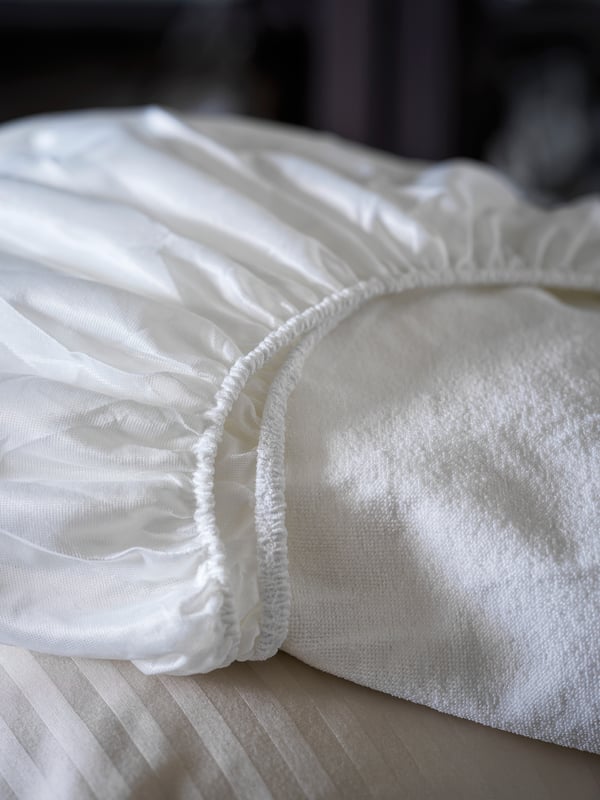 Un cubre colchón GRUSNARV impermeable doblado sobre una cama.