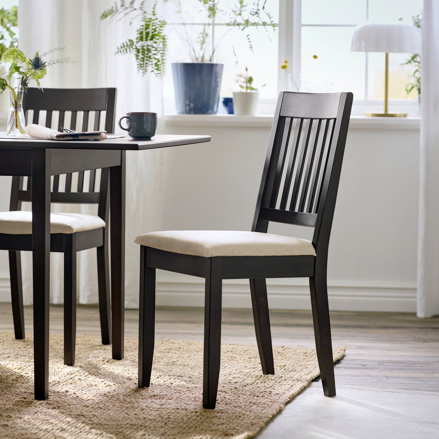 A dark brown NÄSINGE chair with light beige cushion, set beside a dining table in a bright, airy room.