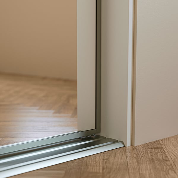 A close-up of a bottom corner of a SKYTTA sliding door solution, mounted with white SKYTTA stop bars against the wall.