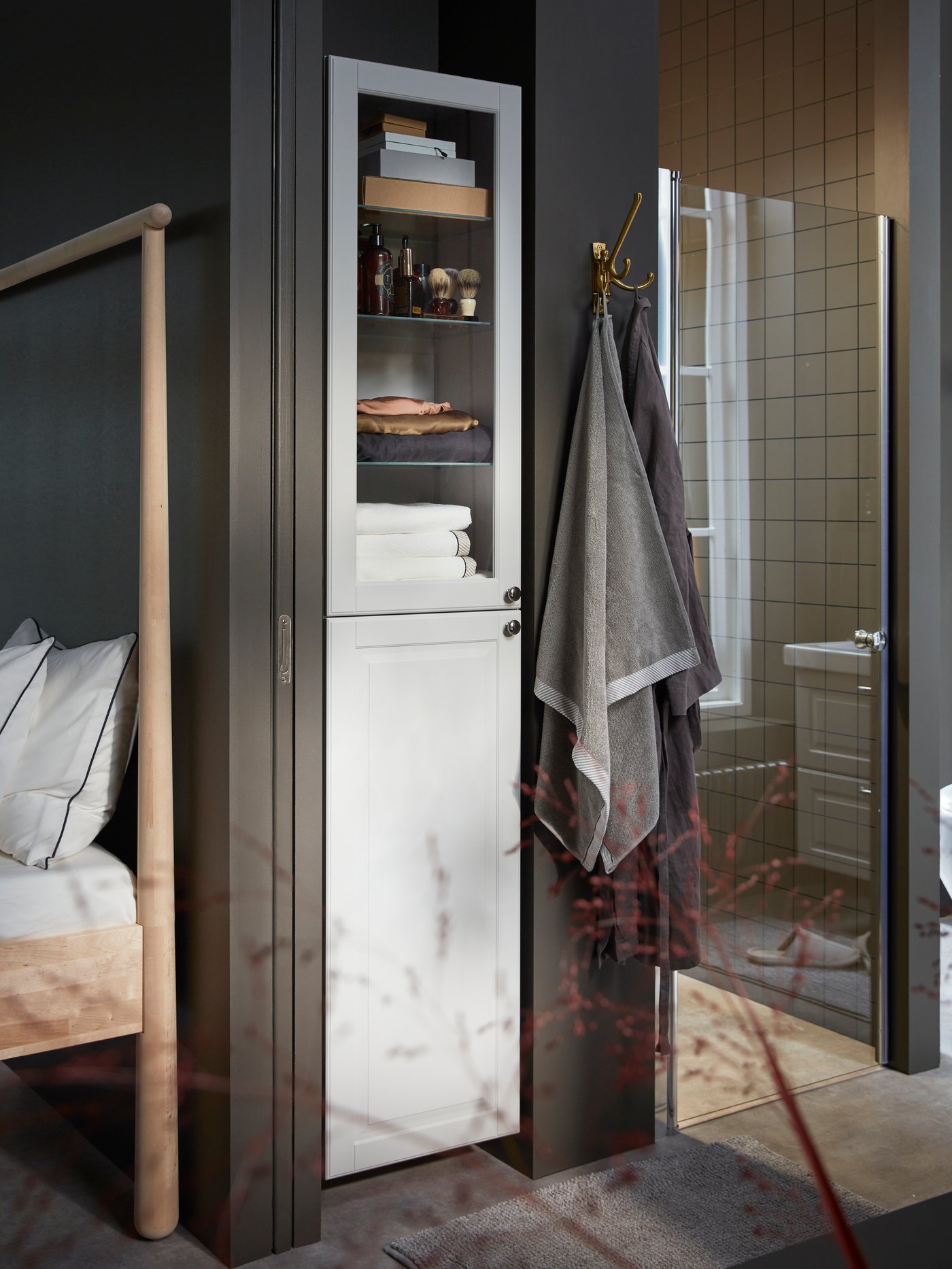 GODMORGON high cabinet in light grey with a glass door revealing towels, storage boxes and shaving products inside.