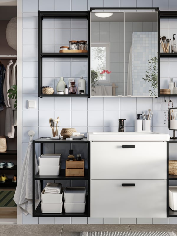 A bathroom has a white ENHET base cabinet with black handles, black base frames with shelves and a mirror glass door cabinet.
