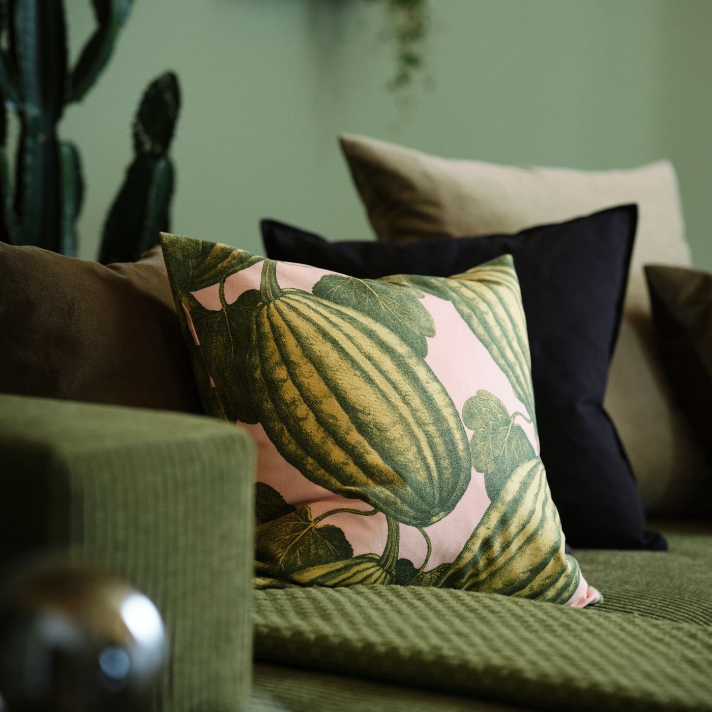 Tre puder i mønster og jordnære farver på en grøn sofa.