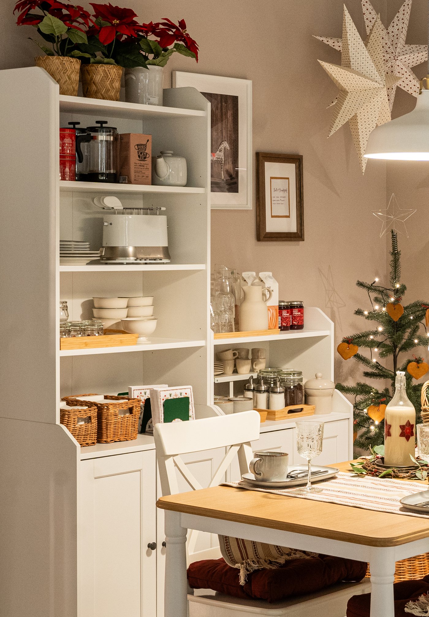 Ein weißer HAUGA Hochschrank mit Vitrinentüren, offenen Regalfächern und Schubladen, dekoriert mit Geschirr, Büchern, Pflanzen und Aufbewahrungsboxen in einem gemütlichen Essbereich.