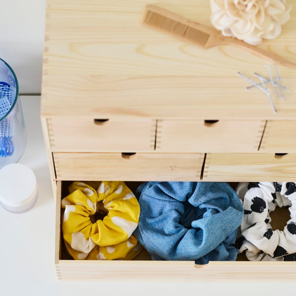 Mini commode MOPPE en pin avec le tiroir du bas ouvert sur trois rangées de chouchous de différentes couleurs.
