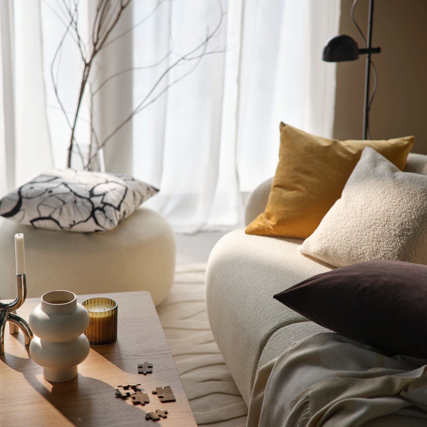 Ein hellbeiges Sofa mit SANELA Kissenbezügen und einer PERSIKOTRÄD Decke neben einem Couchtisch mit einer TOFSTÄRNA Duftkerze.