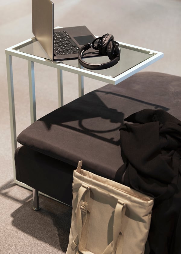 Närbild på ett vitt VITTSJÖ laptopstativ med en uppfälld laptop på. Vid sidan skymtas en mörkgrå SÖDERHAMN fotpall. 