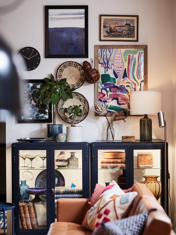 A LANDSKRONA sofa with two FABRIKÖR glass-door cabinets with objects inside in the background, with art on the wall.