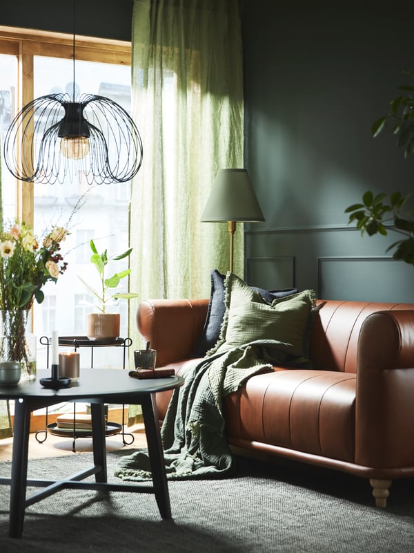 Ein schwarzer KRAGSTA Couchtisch steht unter einer KALLFRONT/HEMMA Pendelleuchte vor einem braunen VISKAFORS 2-Sitzer-Sofa aus Leder.