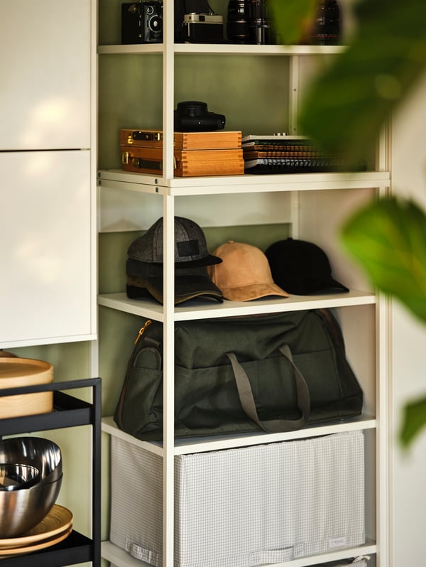 Wit PLATSA open element met planken, met analoge camera’s op de bovenste plank en petten, notitieboeken en een tas op de onderste planken.