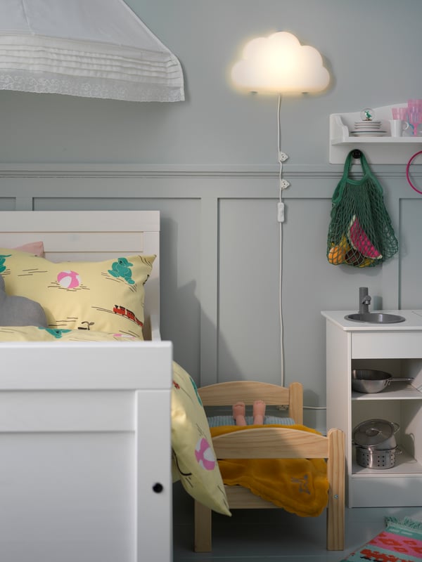 A SUNDVIK extendable bed with colourful KÄPPHÄST bed linen stands under a canopy and near an UPPLYST LED wall lamp.