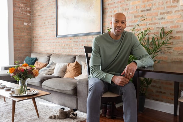 A man sits in a neat and tidy living room, smiling and looking at camera.