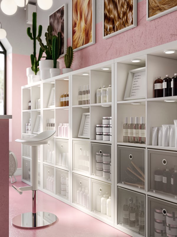Four KALLAX shelving units with five cactuses on top against a pink wall, filled with hair products and storage boxes.