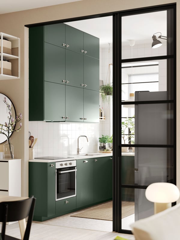 A wide doorway into a kitchen with deep green HAVSTORP kitchen fronts and a white marble effect/laminate EKBACKEN worktop.