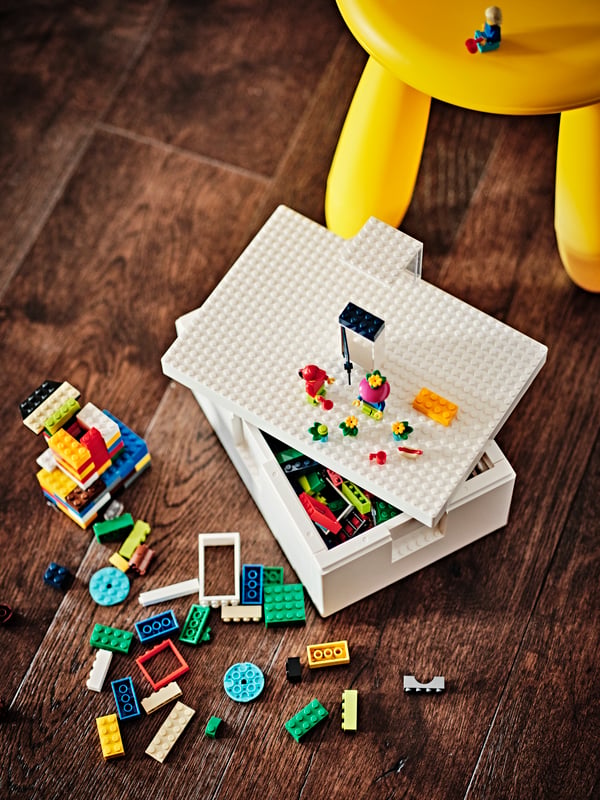 Una caja BYGGLEK de IKEA sonre un piso de madera. A los costados hay muchos bloques de LEGO de diferentes formas y colores.