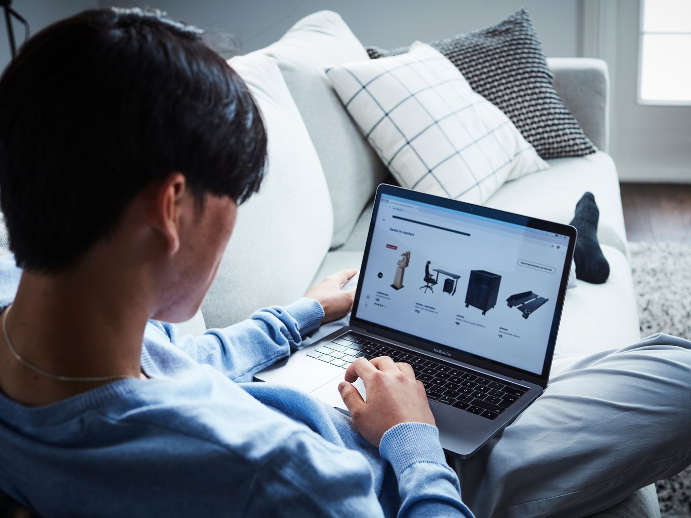 A person relaxes on the sofa while browsing IKEA products on a laptop from home.
