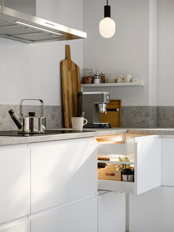A kitchen corner in a kitchen with smooth white VOXTORP fronts. One top drawer is pulled out, showing things stored inside.