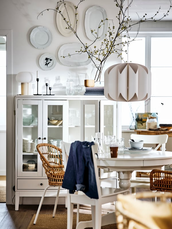 A white dining room containing an IDANÄS glass-door cabinet, and an INGATORP table with white and rattan chairs around it.