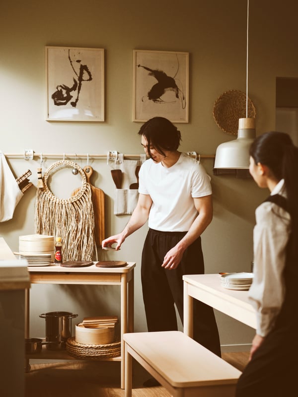A kitchen featuring two people, a RÖNNINGE trolley, BUNKEFLO pendant lamp, a RÖNNINGE extendable table and two RIBBA frames.