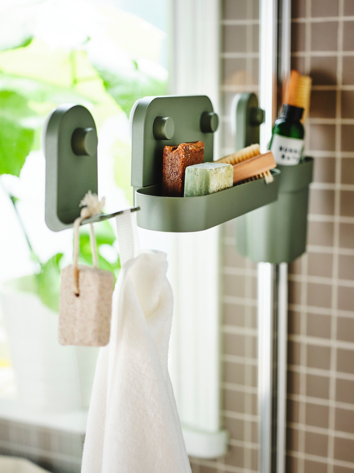 A glass shower screen holds an ÖBONÄS wall shelf with suction cup. Toiletries sit inside, and a hand towel hangs from a hook.