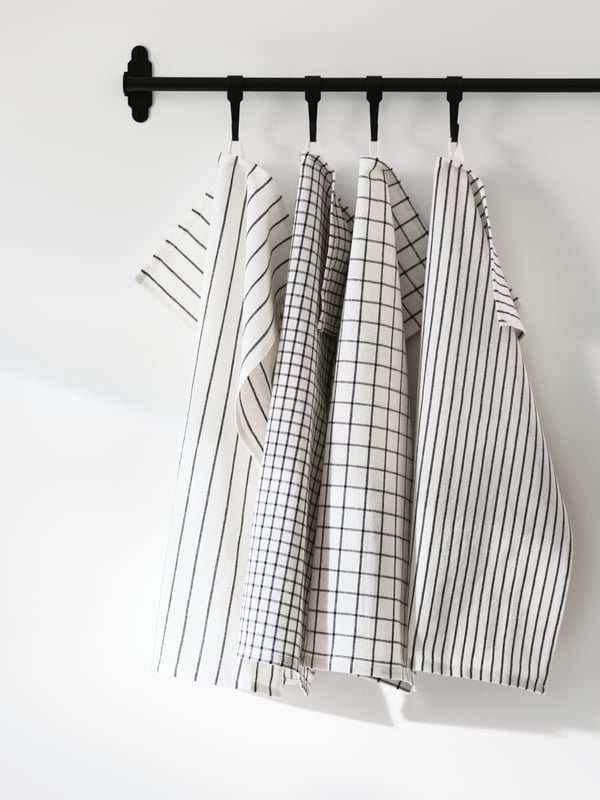 A HULTARP rail in black with four RINNIG tea towels in white and dark grey pattern hanging from HULTARP hooks in black.