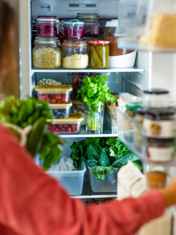 A woman opens a refrigerator, full of healthy greens.