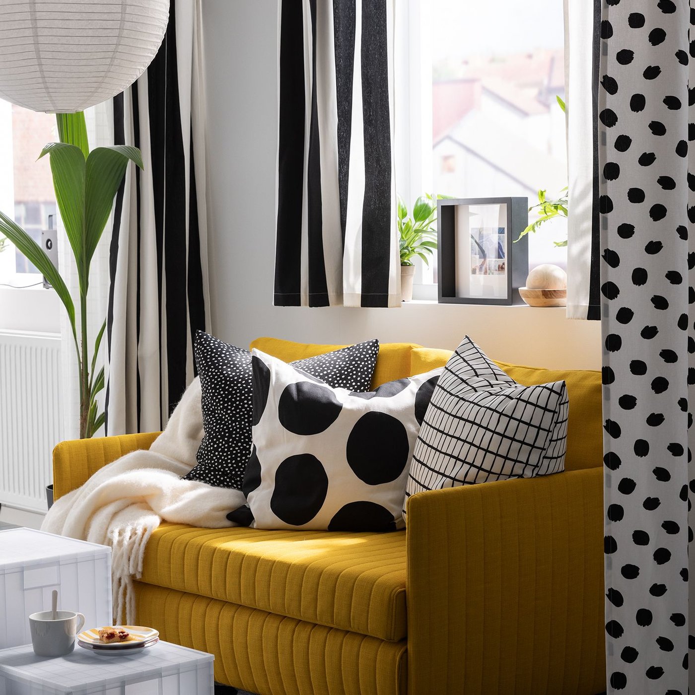 A throw and three cushions, including one with a BLÅMUNKAR cushion cover with large black dots, lie on a FRIDHULT sofa-bed.