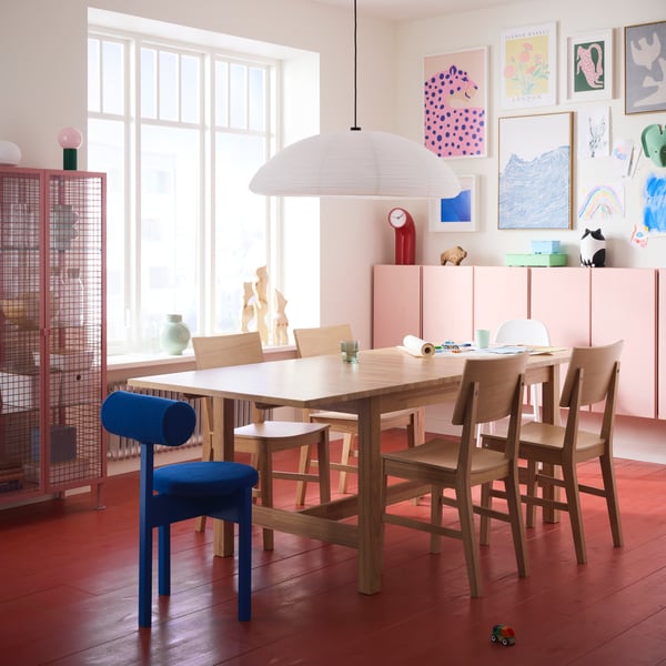 A bright dining area with a red floor features a KARSKÄR extendable table and chairs and colourful artwork on the wall.