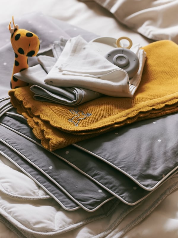 A SOLGUL blanket in dark yellow with an assortment of baby textiles in grey and white together with a small stuffed toy.