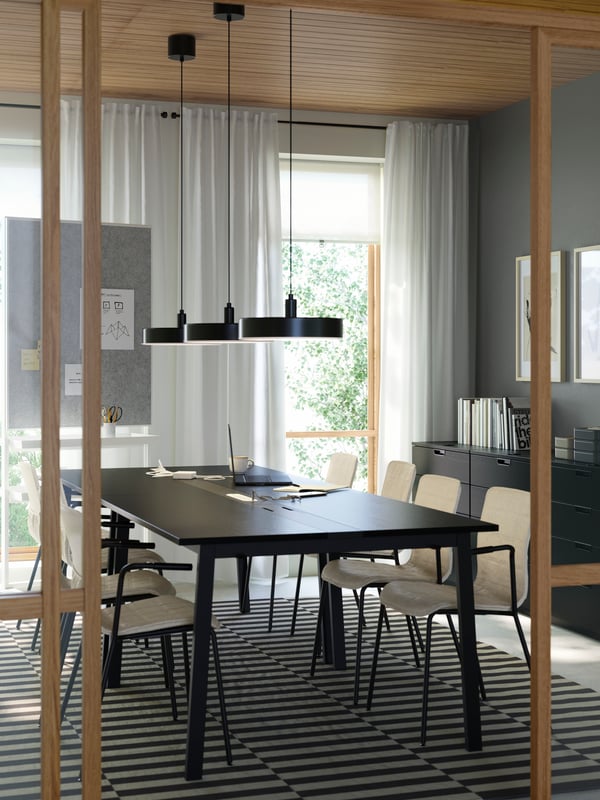 A modern meeting room with four black MITTZON conference tables, six LÄKTARE chairs in light wood and a striped wool rug.