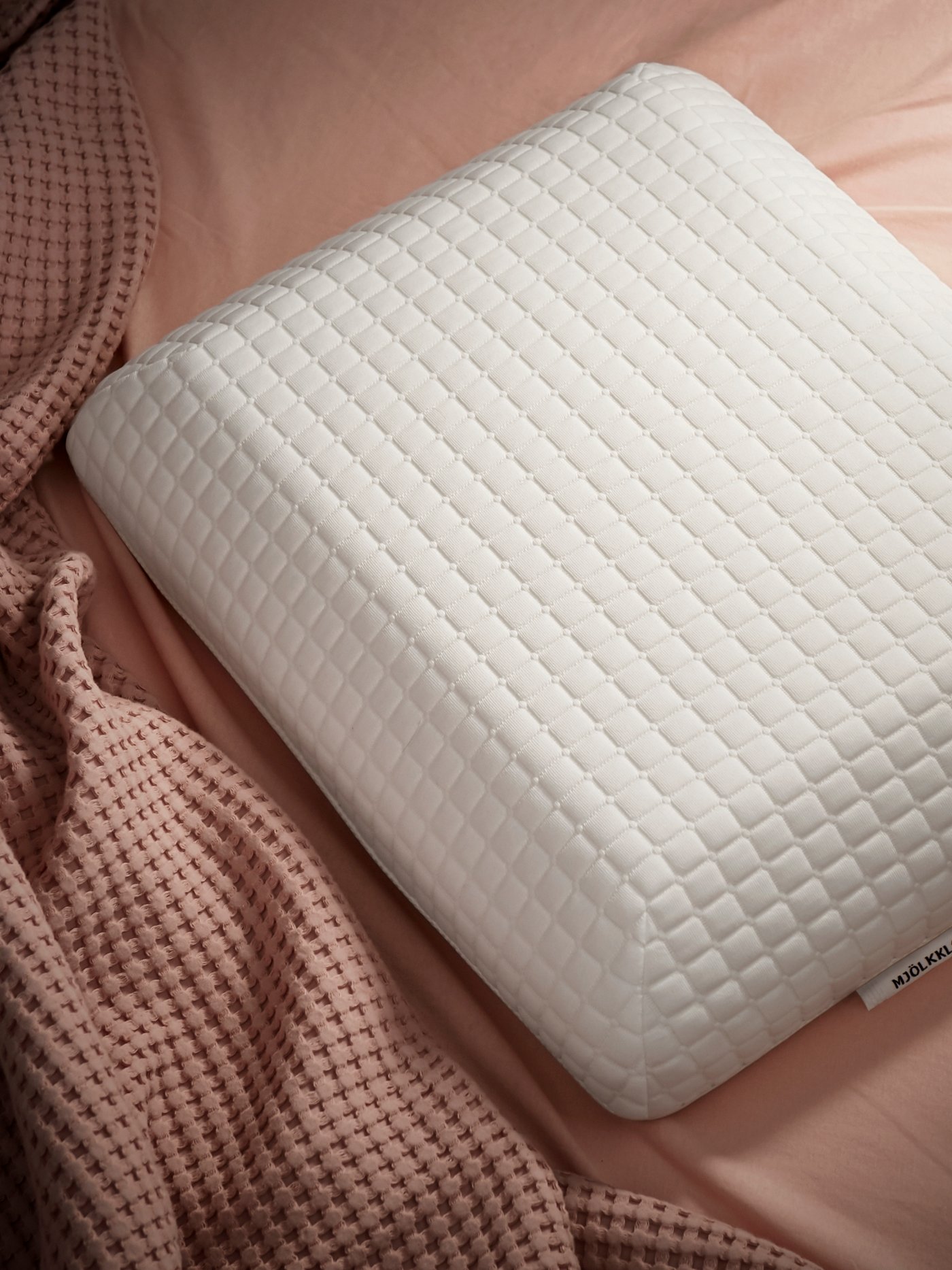 A MJÖLKKLOCKA ergonomic pillow on a bed with light brown bed linen and a light brown blanket.