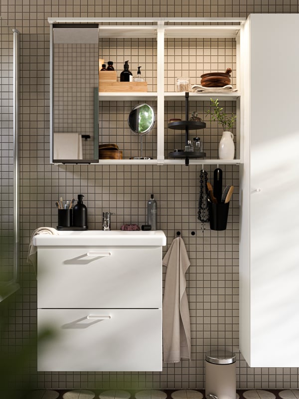 A white ENHET high frame with shelves has grey and white towels, toilet paper rolls and bathroom products on the shelves.