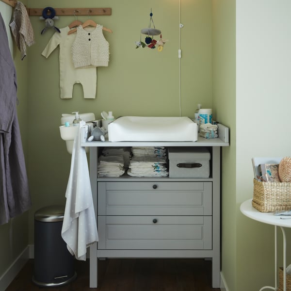 Dans un angle de la pièce est installée une table à langer/commode SUNDVIK grise sur laquelle est posé un matelas à langer VÄDRA.