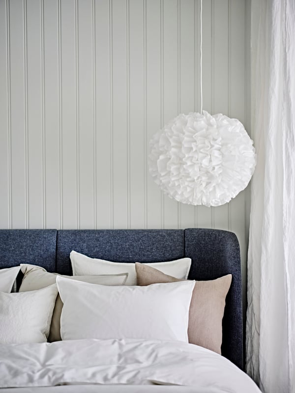 A white VINDKAST pendant lamp above a TUFJORD upholstered bed dressed in a white ÄNGSLILJA duvet cover with 2 pillowcases.