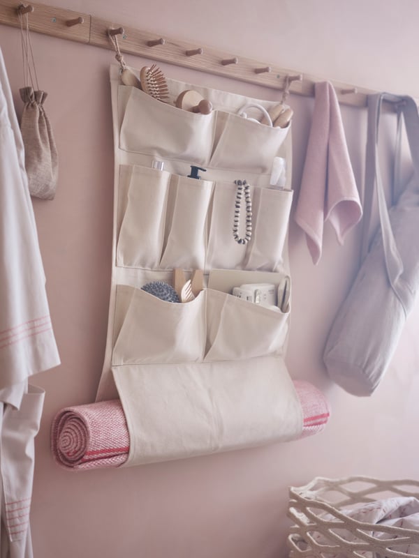 A VÅRDANDE cotton canvas wall organiser hanging on wooden pegs with towels and a canvas bag.