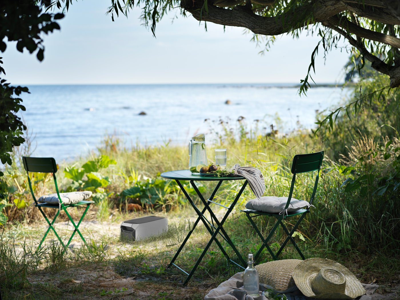 Dans une prairie, on aperçoit un coin de verdure avec vue sur un lac, deux chaises, une table et une station d'alimentation portable.