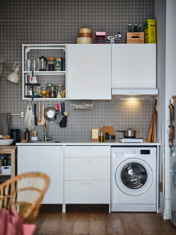 A white ENHET kitchen with open and closed storage on a grey tiled wall, plus a washing machine and various cooking items.