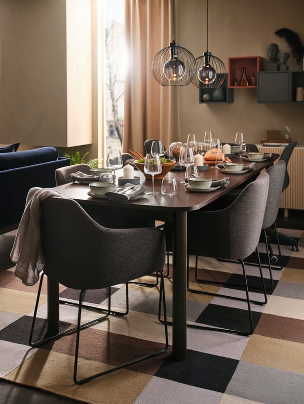 A STRANDTORP extendable table set for dinner, surrounded by TOSSBERG and LÅNGFJÄLL chairs, with two pendant lamps above.