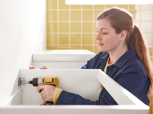 En IKEA-medarbejder monterer et toilet på en badeværelsesvæg med en skruetrækker.