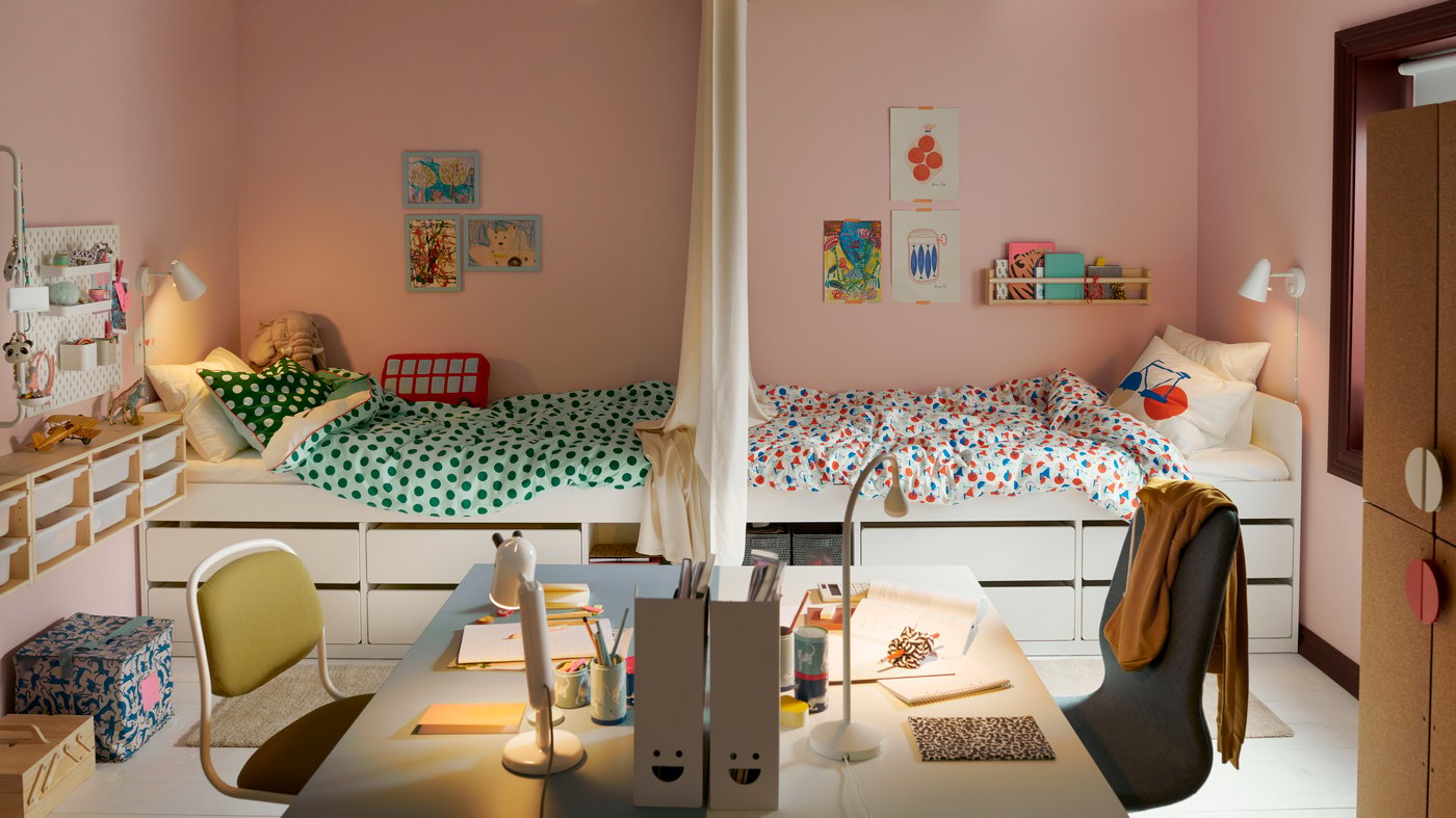 A shared children’s bedroom divided in two with the beds facing each other and in the foreground two desks facing each other.
