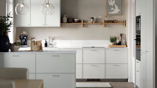 Modernt kök med vita skåpluckor, köksö, öppna hyllor och glaspendlar över arbetsytan i ljusa, neutrala toner.
