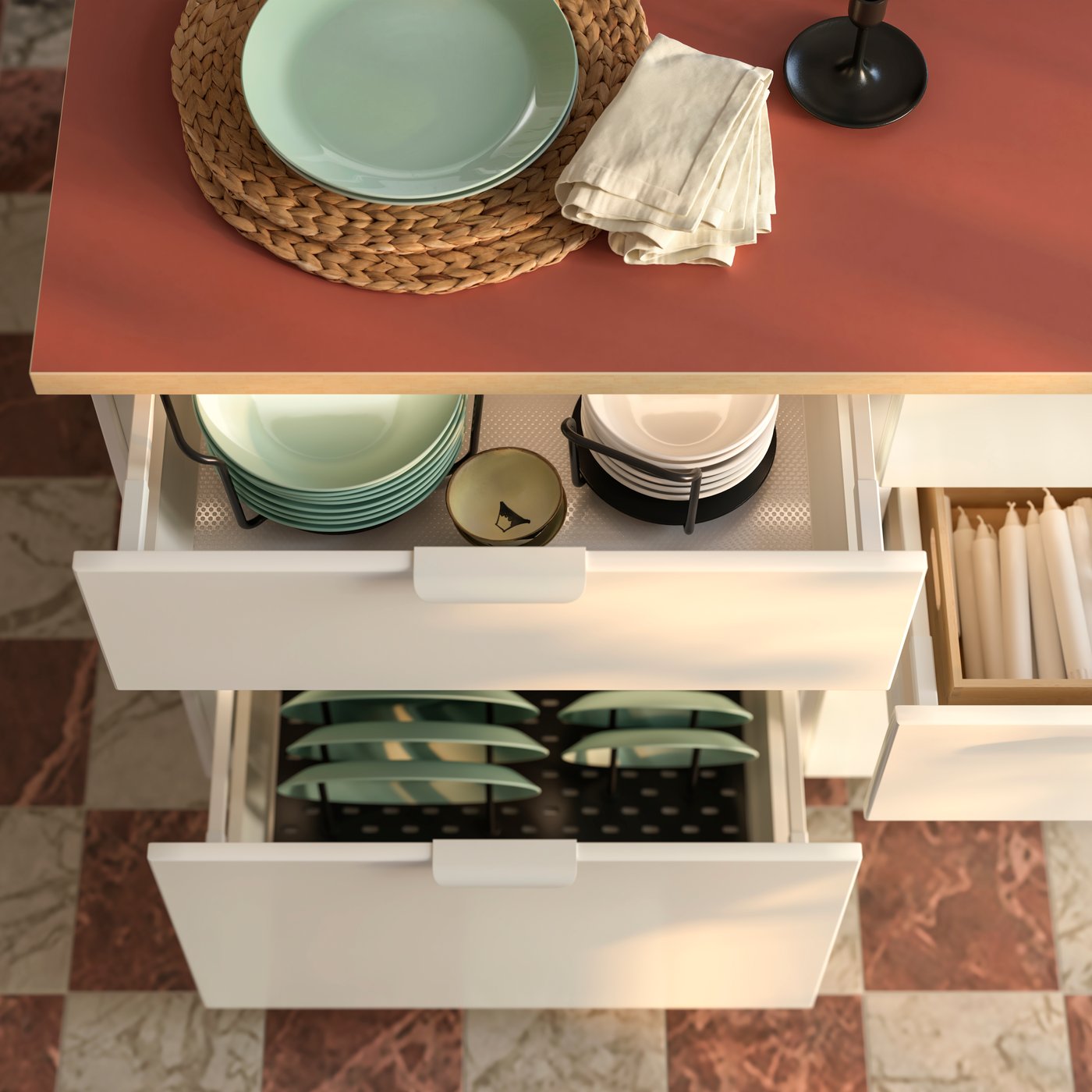 A stylish kitchen featuring a pink countertop, white drawers filled with green plates, and a woven placemat beneath a plate.