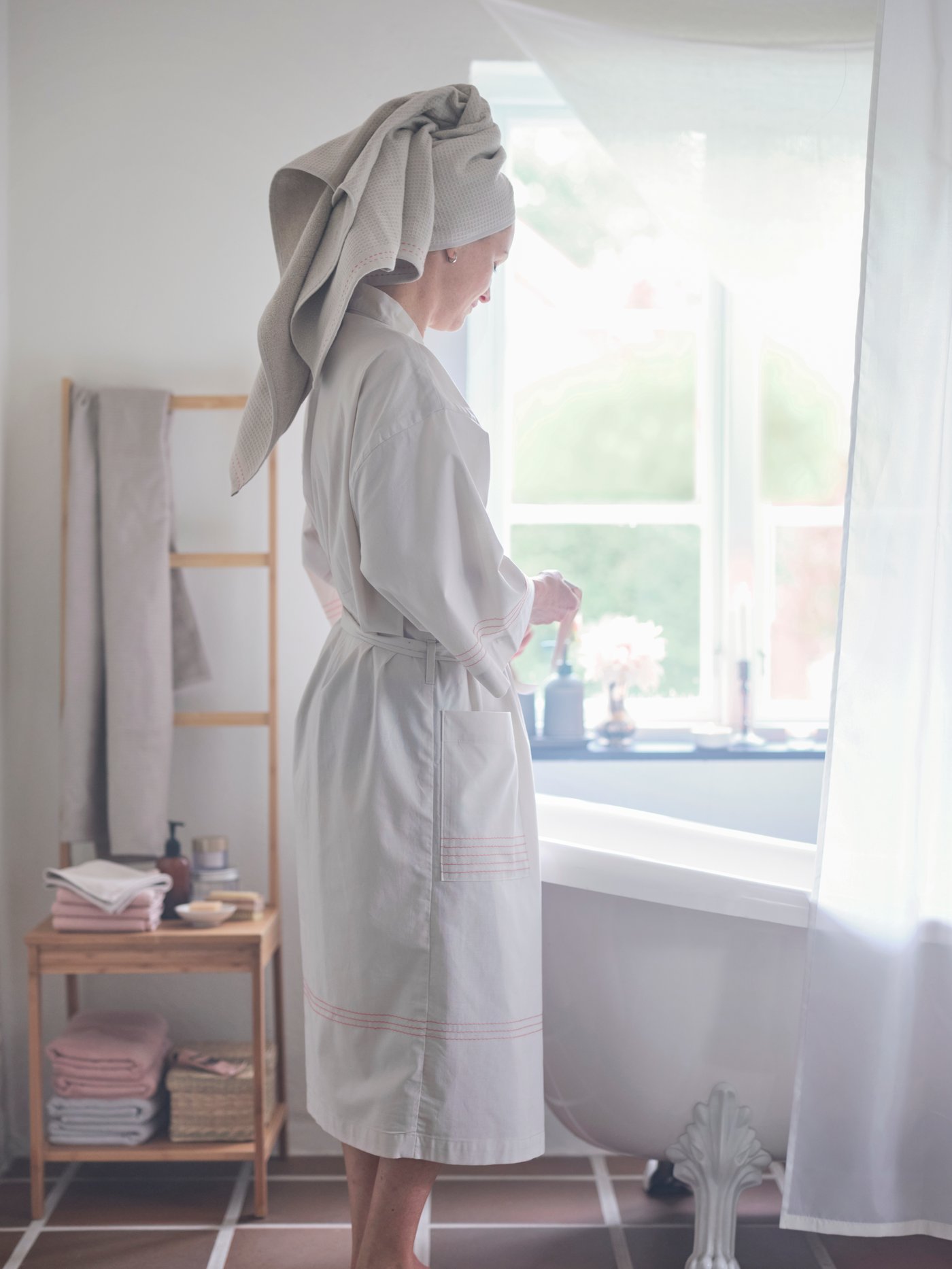 A woman wearing a VÅRDANDE cotton kimono uses a VÅRDANDE towel as a turban to dry her hair in a bathroom.