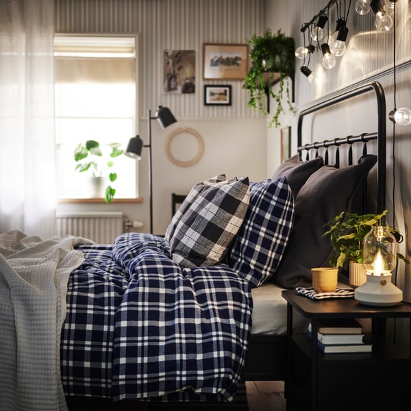 Bed seen from the side with bedside table in foreground and a window and floor lamp in back. TORNTUSS blue/white bedding.