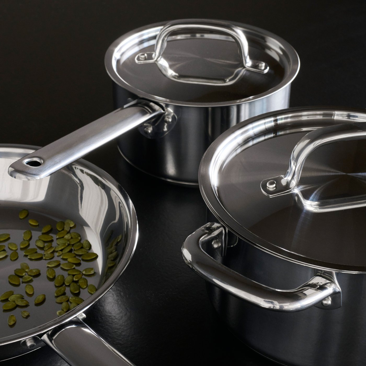 One large IKEA 365+ frying pan containing pumpkin seeds next to two smaller KEA 365+ saucepans with their lids on.