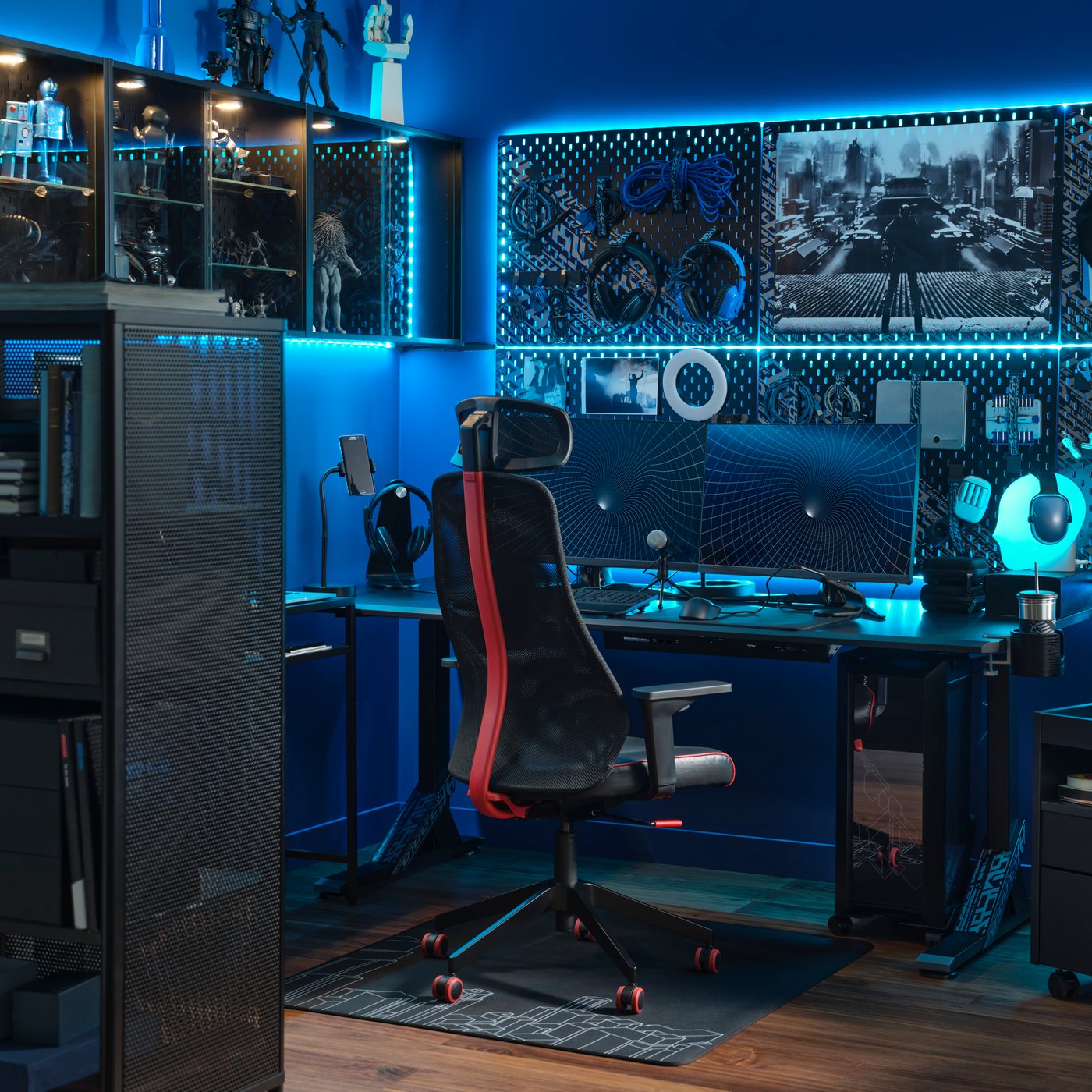Gaming room lit with blue light is furnished with two monitors, gaming chair, desk, cabinetry, peg boards, and a variety of gaming accessories.