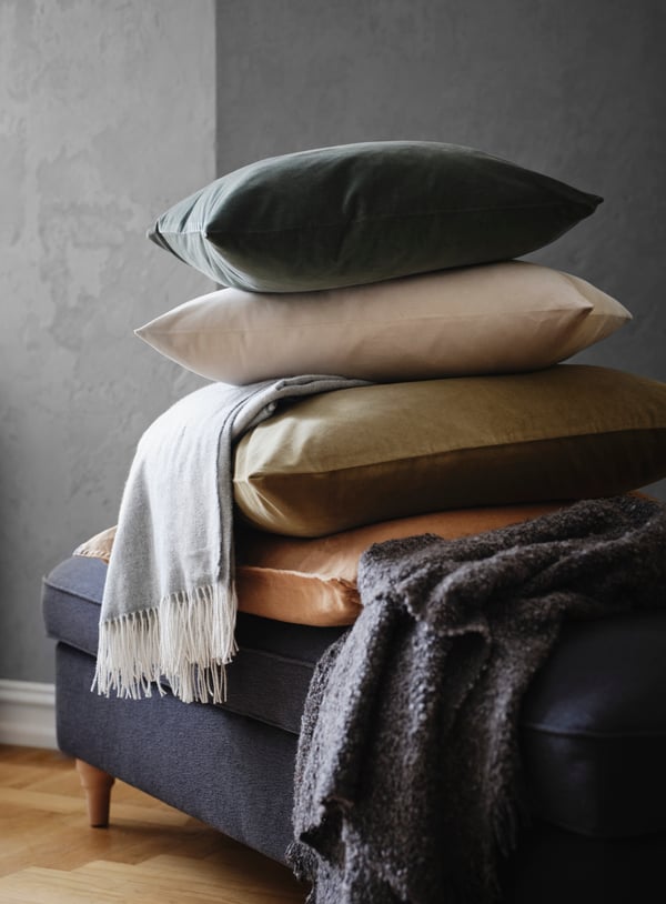 ESSEBODA footstool in anthracite with a pile of cushions in different colours like olive-green, grey-green and light beige.